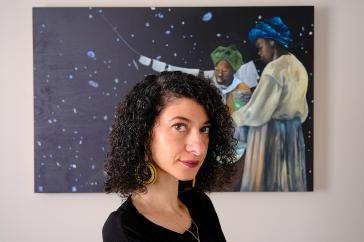 Chanda Prescod-Weinstein looks at the camera in front of a painting